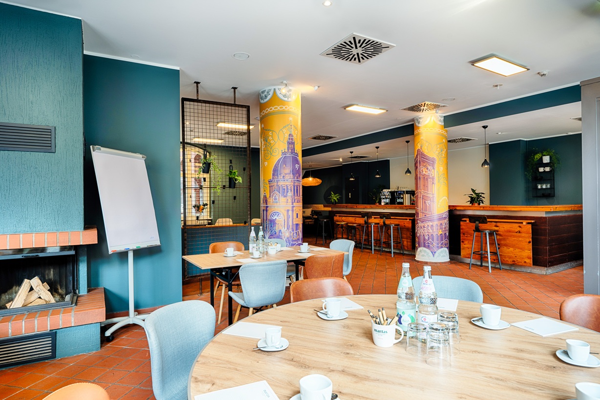 Blick in Veranstaltungsraum mit einem runden bestulten Tisch im Vordergrund